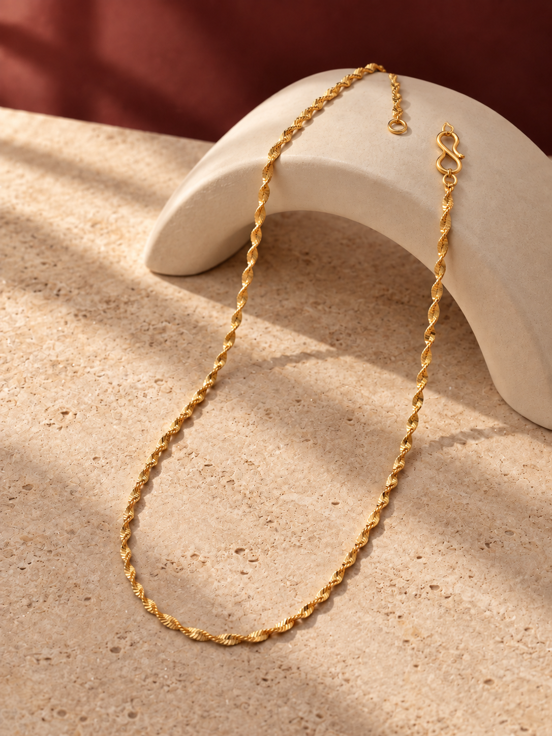 Twisted gold plated chain draped over cream stone arch in soft sunlight