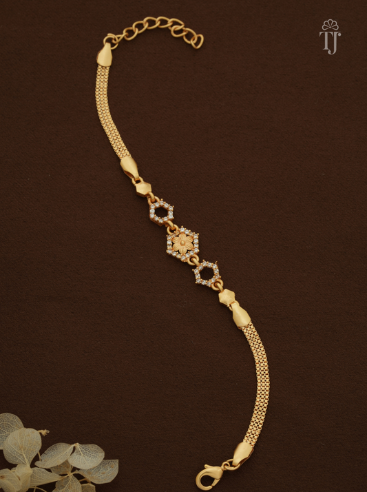 A gold chain bracelet with a central diamond-shaped motif set with small clear stones and two circular diamond-shaped links, displayed on a dark brown textured background with a decorative floral corner.