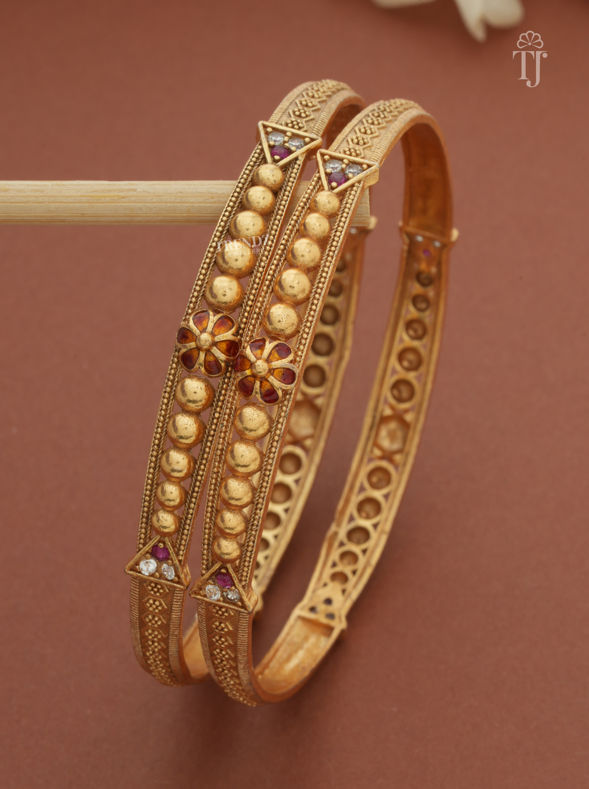 Close-up of meena work flower with pink and white stones on antique finish bangles