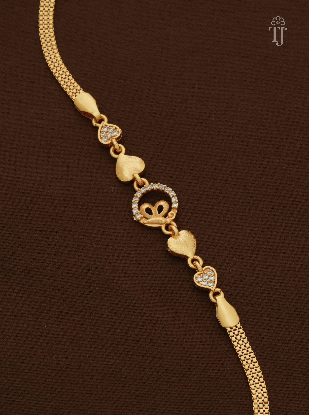A gold heart-link chain bracelet with a central heart-and-crown motif set with small clear stones, displayed on a dark brown textured background.