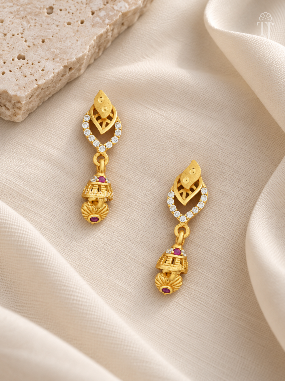 Pair of gold plated double leaf earrings with pink stone jhumka on cream linen
