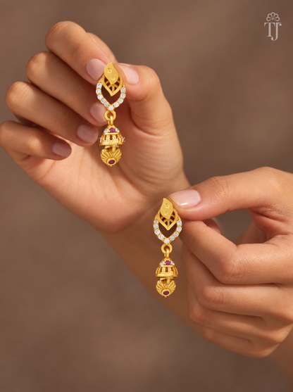 Fingers holding gold plated double leaf earrings with mini jhumka