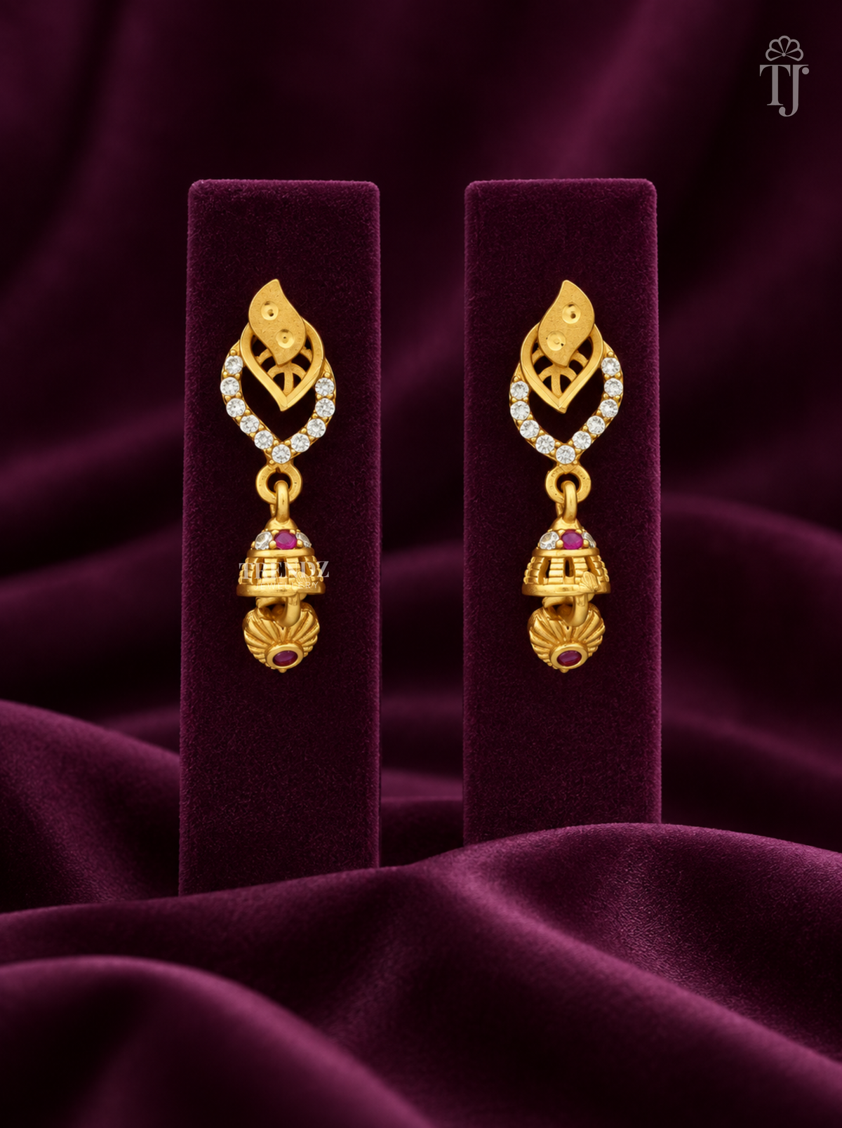 Gold plated double leaf jhumka earrings with AD stones on plum velvet display stand