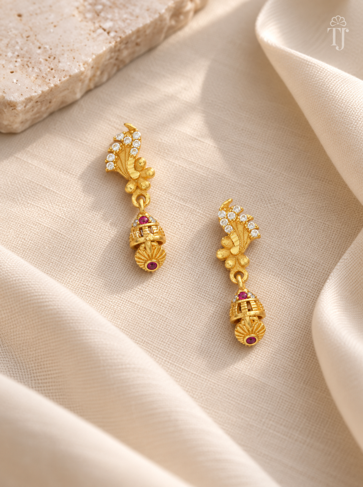 Pair of gold plated feather design earrings with pink stone jhumka on cream linen