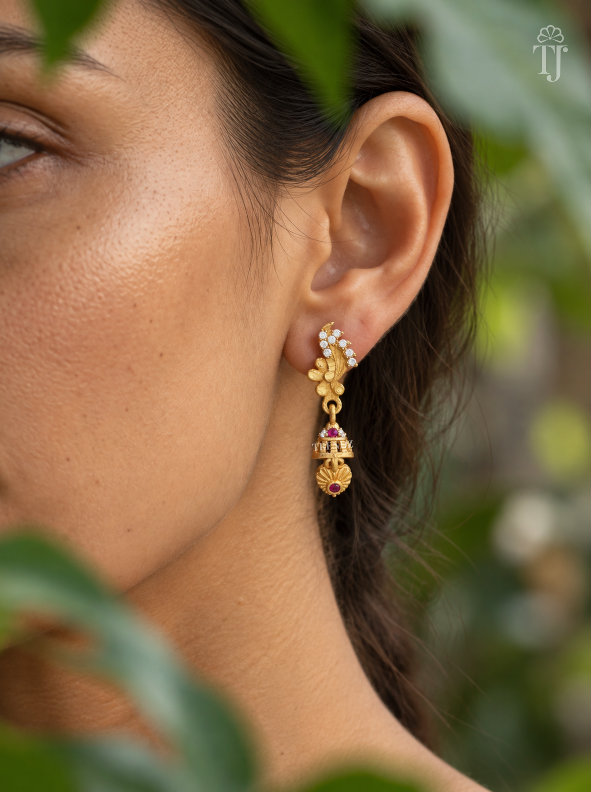 Side view of woman wearing gold plated feather design jhumka drop earrings