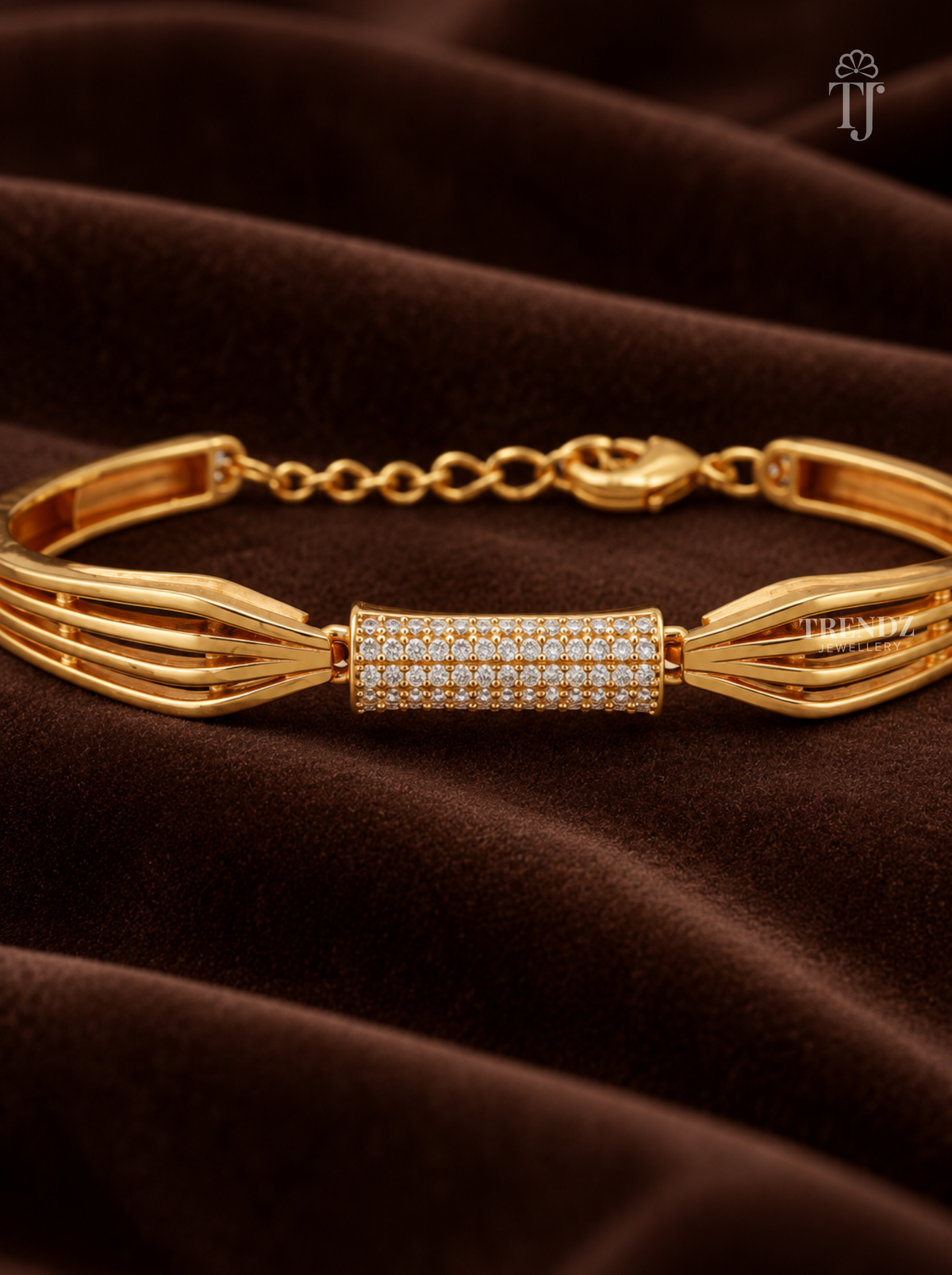A gold-toned multi-strand bracelet with a central pavé diamond cylinder, displayed on a draped dark brown velvet fabric background.