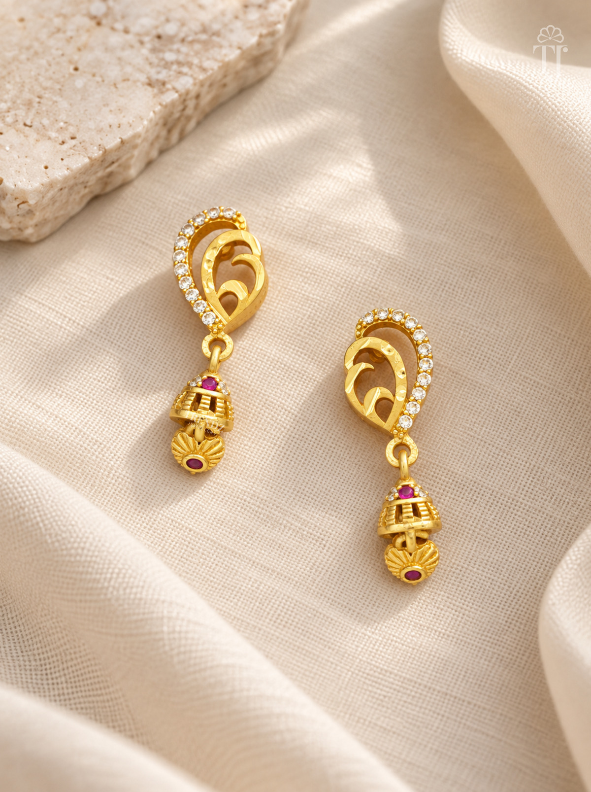 Pair of gold plated mango design drop earrings with pink stone on cream linen