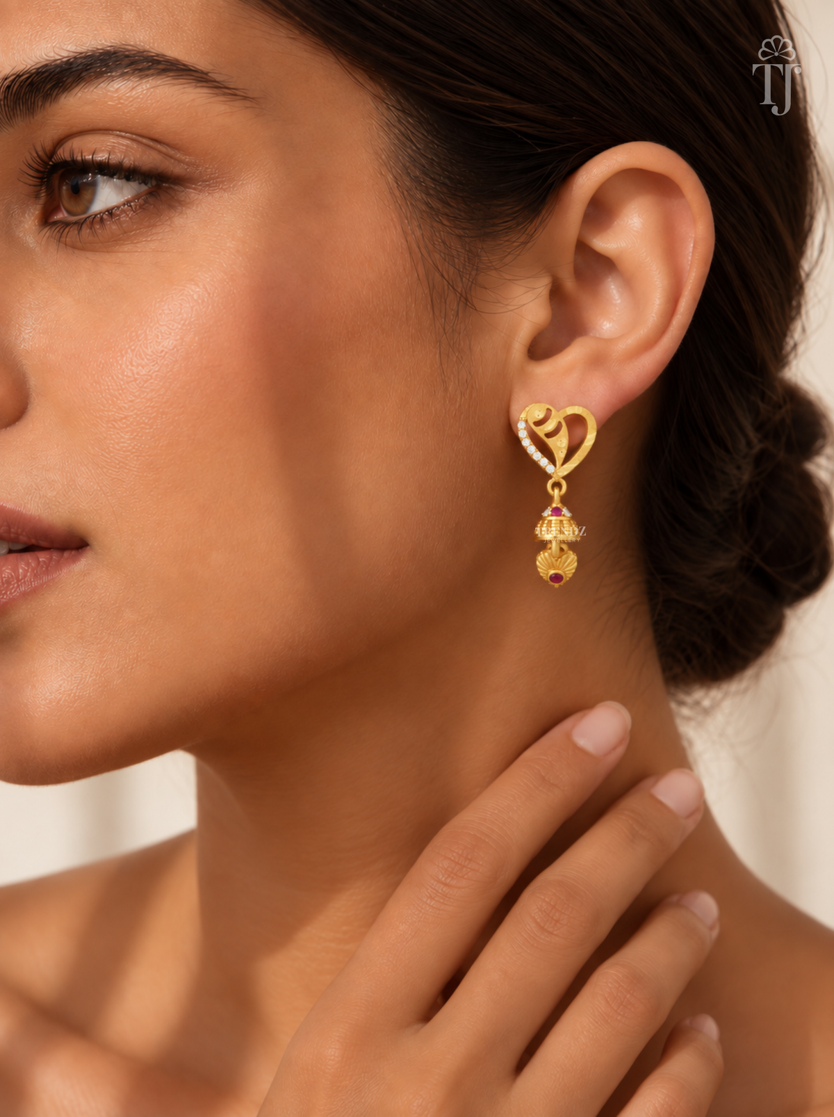 Woman wearing small gold plated heart design jhumka earrings with AD stones