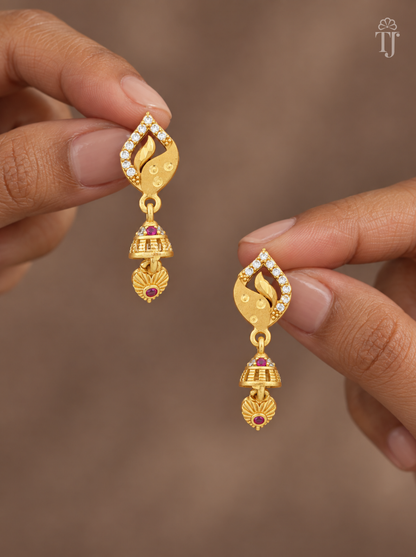 Fingers holding gold plated leaf design earrings with pink stone jhumka