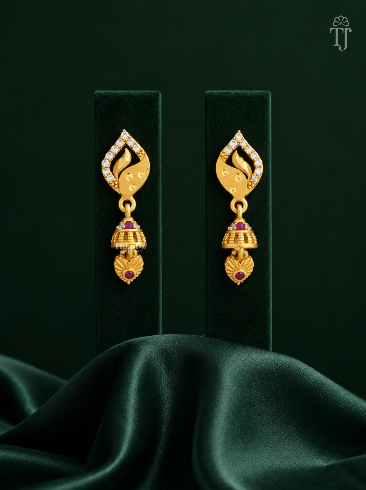 Gold plated leaf design jhumka earrings with AD stones on dark green display stand