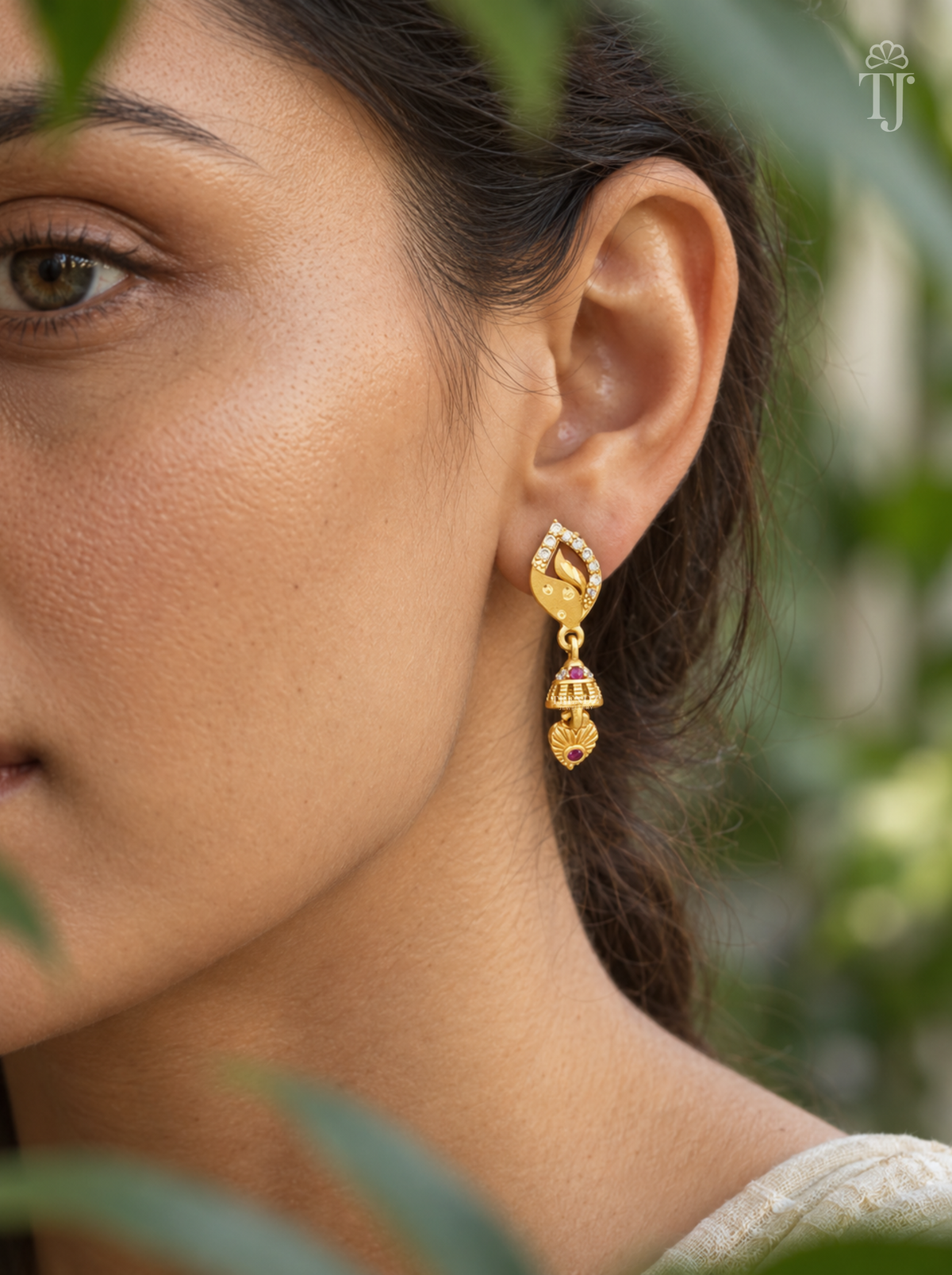 Side view of woman wearing gold plated leaf design jhumka drop earrings