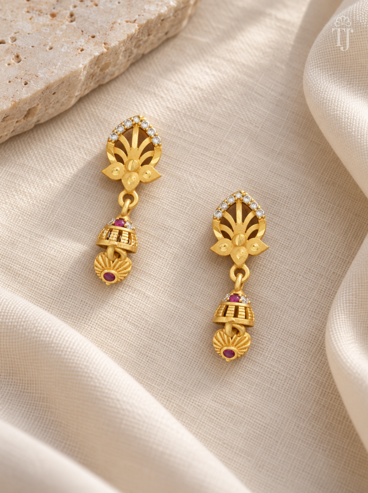 Pair of gold plated lotus design earrings with pink stone jhumka on cream linen