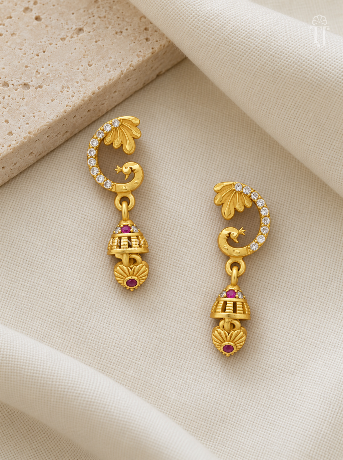Pair of gold plated peacock design earrings with pink stone jhumka on cream linen