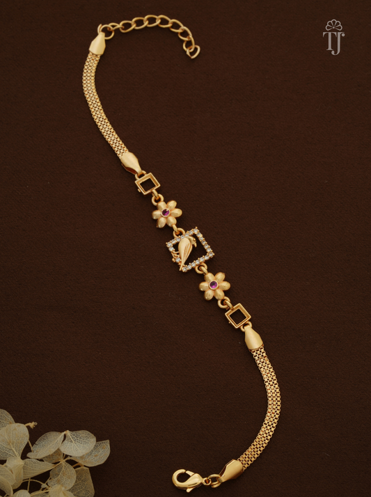 A gold chain bracelet with a central square frame featuring a horse motif, accented by small flower charms with pink and white petals, and set against a dark brown background.