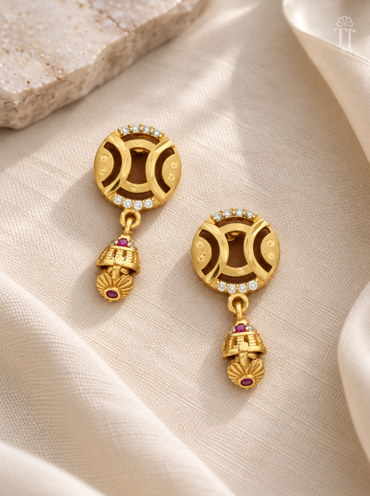 Pair of gold plated round earrings with pink stone jhumka on cream linen
