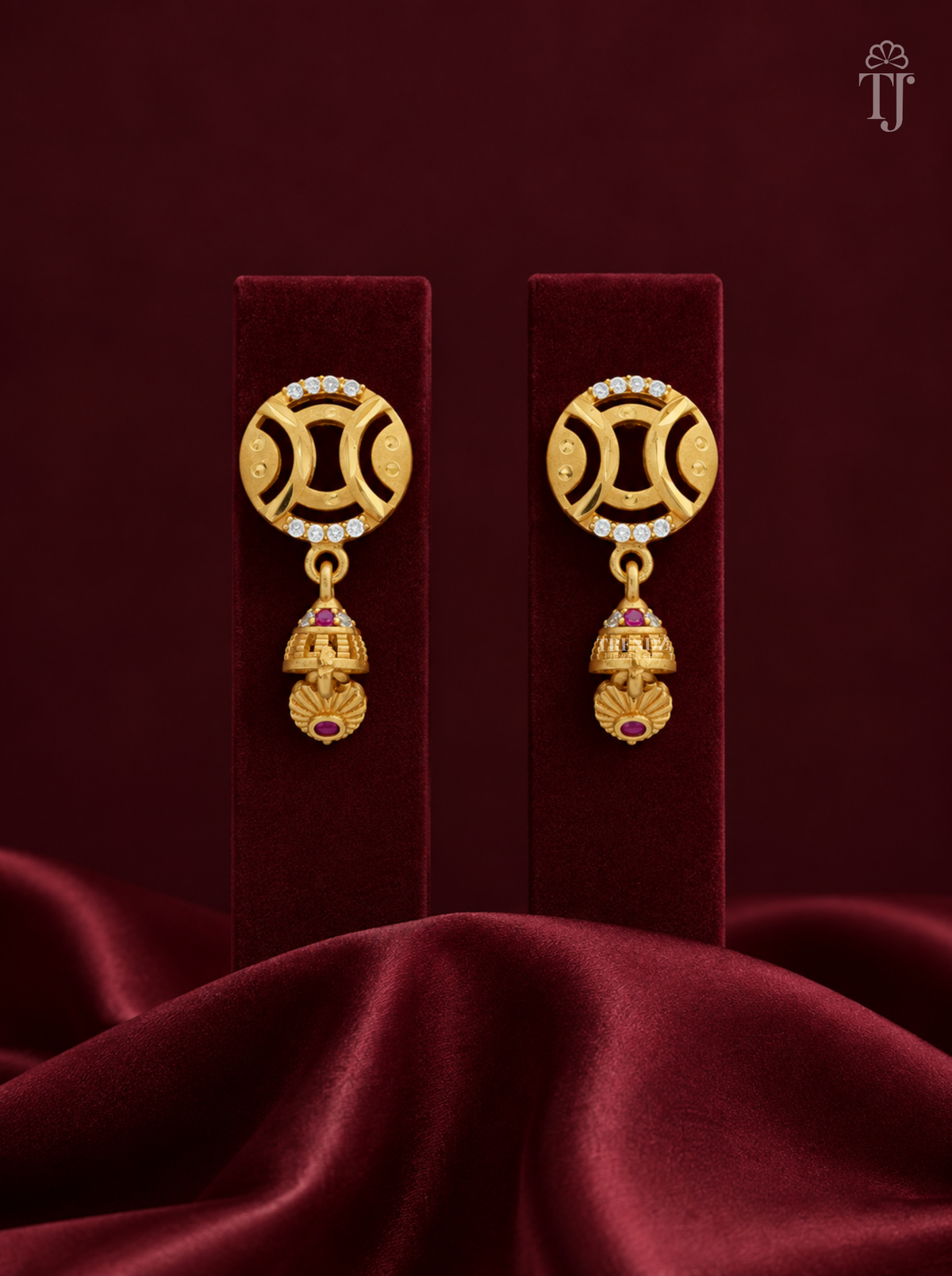 Gold plated round jhumka earrings with AD stones on maroon velvet display stand