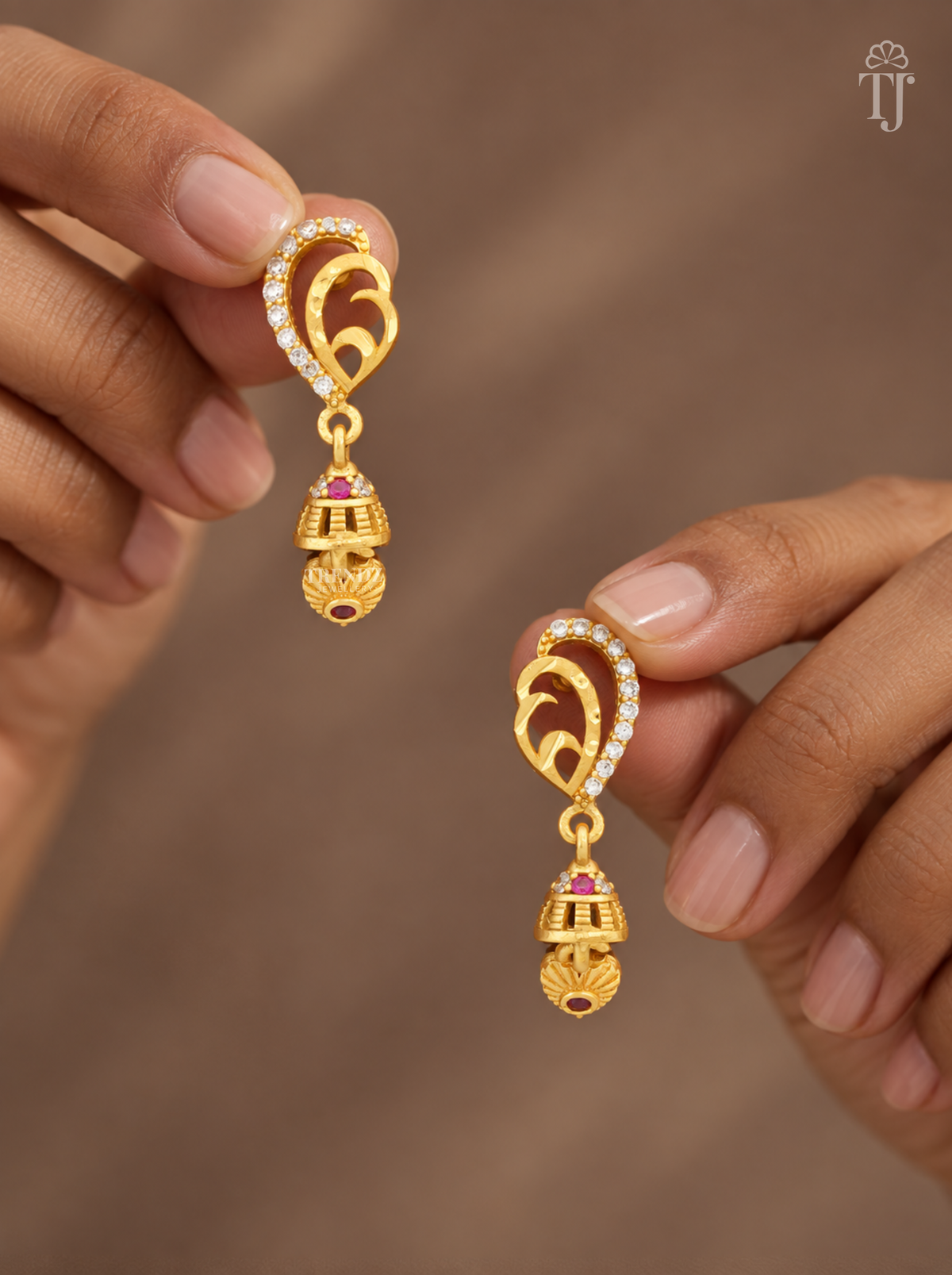 Fingers holding gold plated mango design earrings with AD stones and mini jhumka