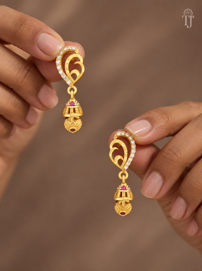 Fingers holding gold plated mango design earrings with AD stones and mini jhumka