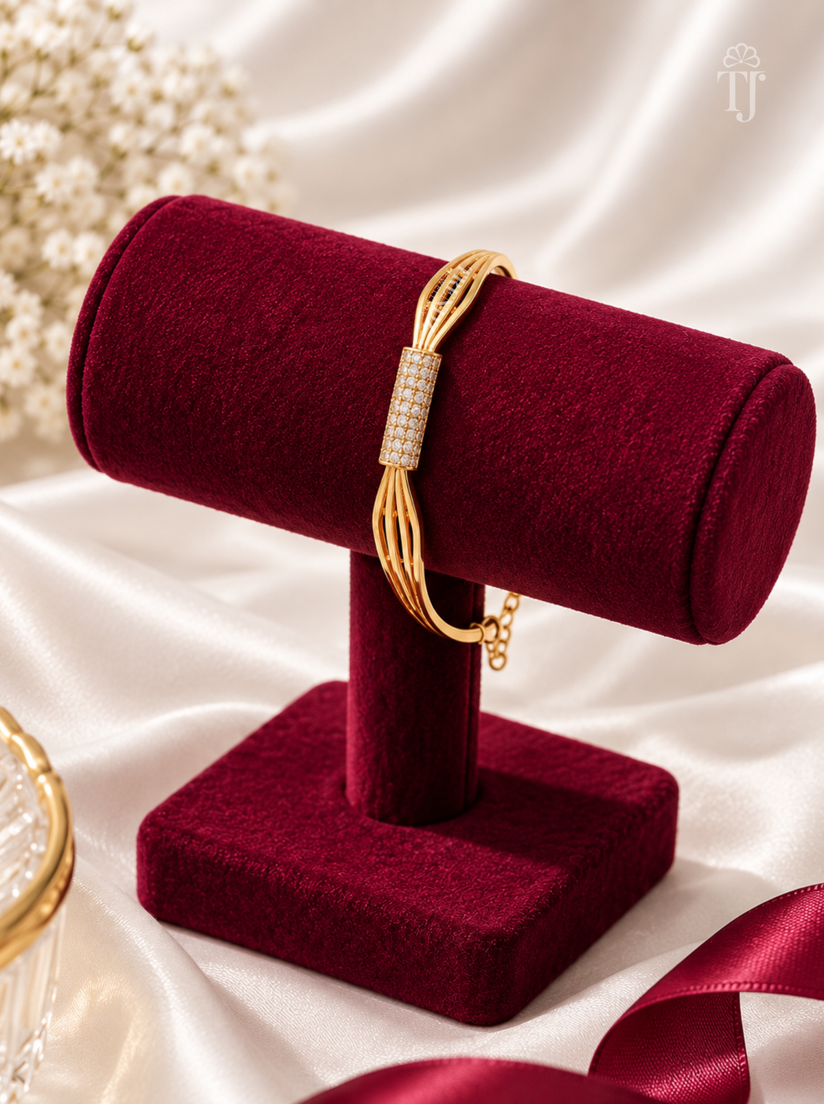 A gold-toned bracelet with a rectangular pavé-set stone center, displayed on a deep burgundy velvet jewelry stand against a soft white satin backdrop.