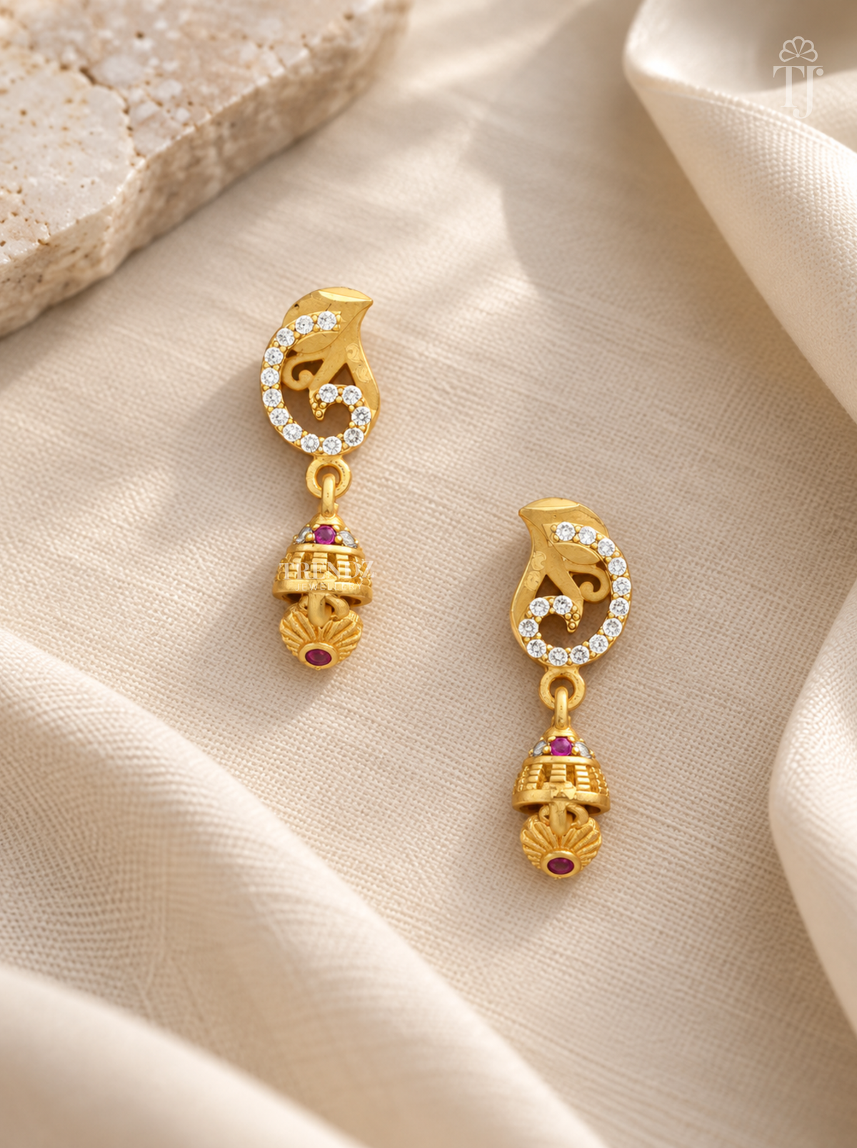 Pair of gold plated swirl design earrings with pink stone jhumka on cream linen