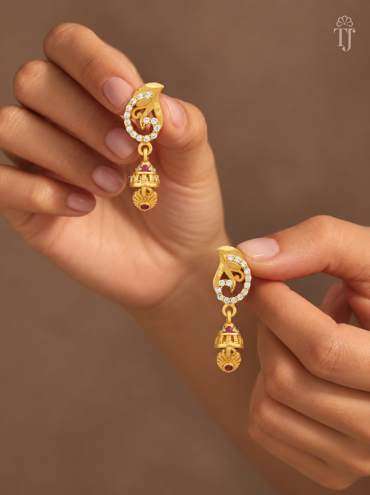 Fingers holding gold plated swirl design earrings with mini jhumka
