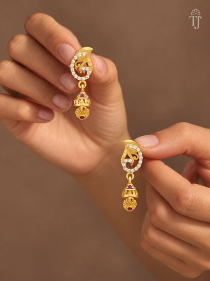 Fingers holding gold plated swirl design earrings with mini jhumka