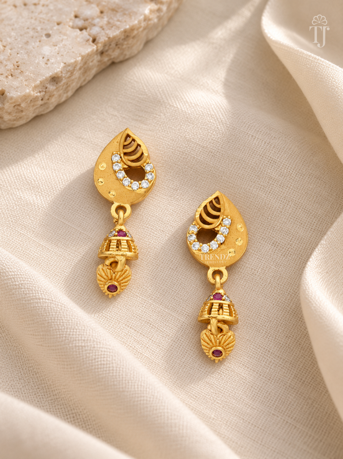 Pair of gold plated teardrop earrings with heart-shaped drop on cream linen