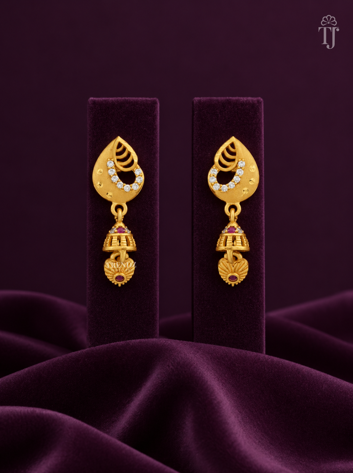 Gold plated teardrop jhumka earrings with AD stones on purple velvet display stand