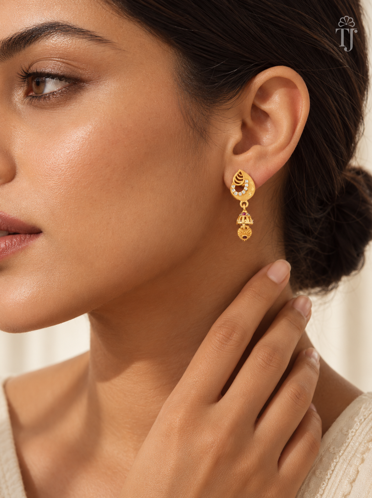 Woman wearing small gold plated teardrop jhumka earrings with AD stones