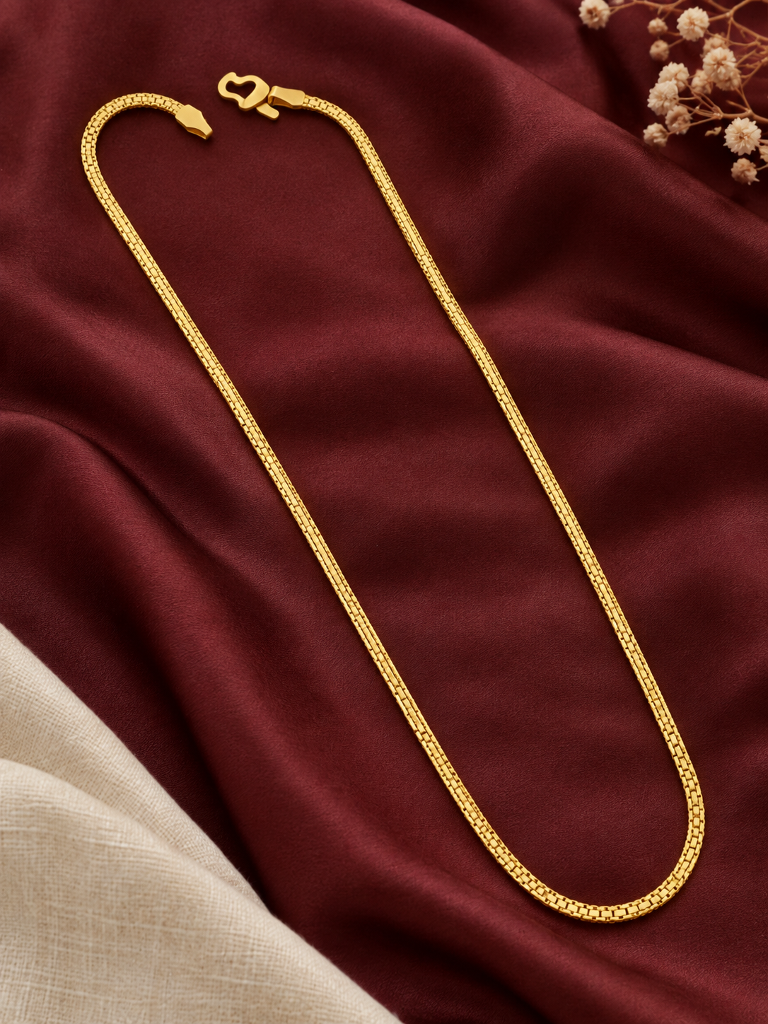 Thin gold plated box link chain laid on maroon fabric with linen and flowers