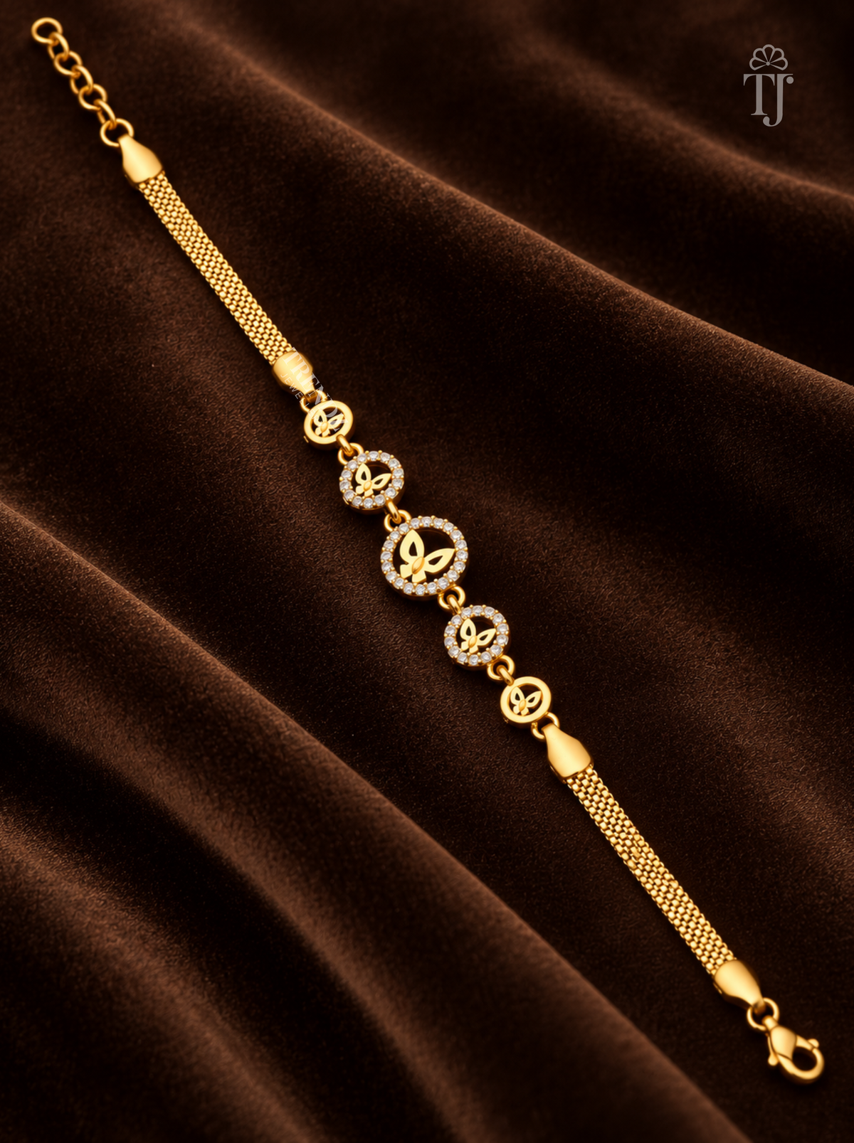 A gold chain bracelet with five central circular motifs, four of which are adorned with small clear stones, displayed on a draped dark brown velvet fabric.