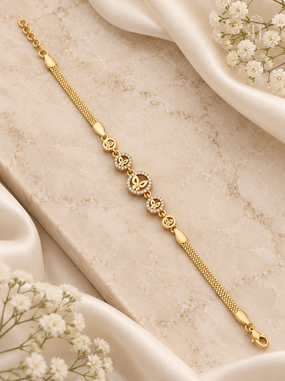 A gold chain bracelet with a central heart-shaped cluster of small clear stones and repeating heart motifs, styled on a beige marble slab with white satin and baby's breath flowers.