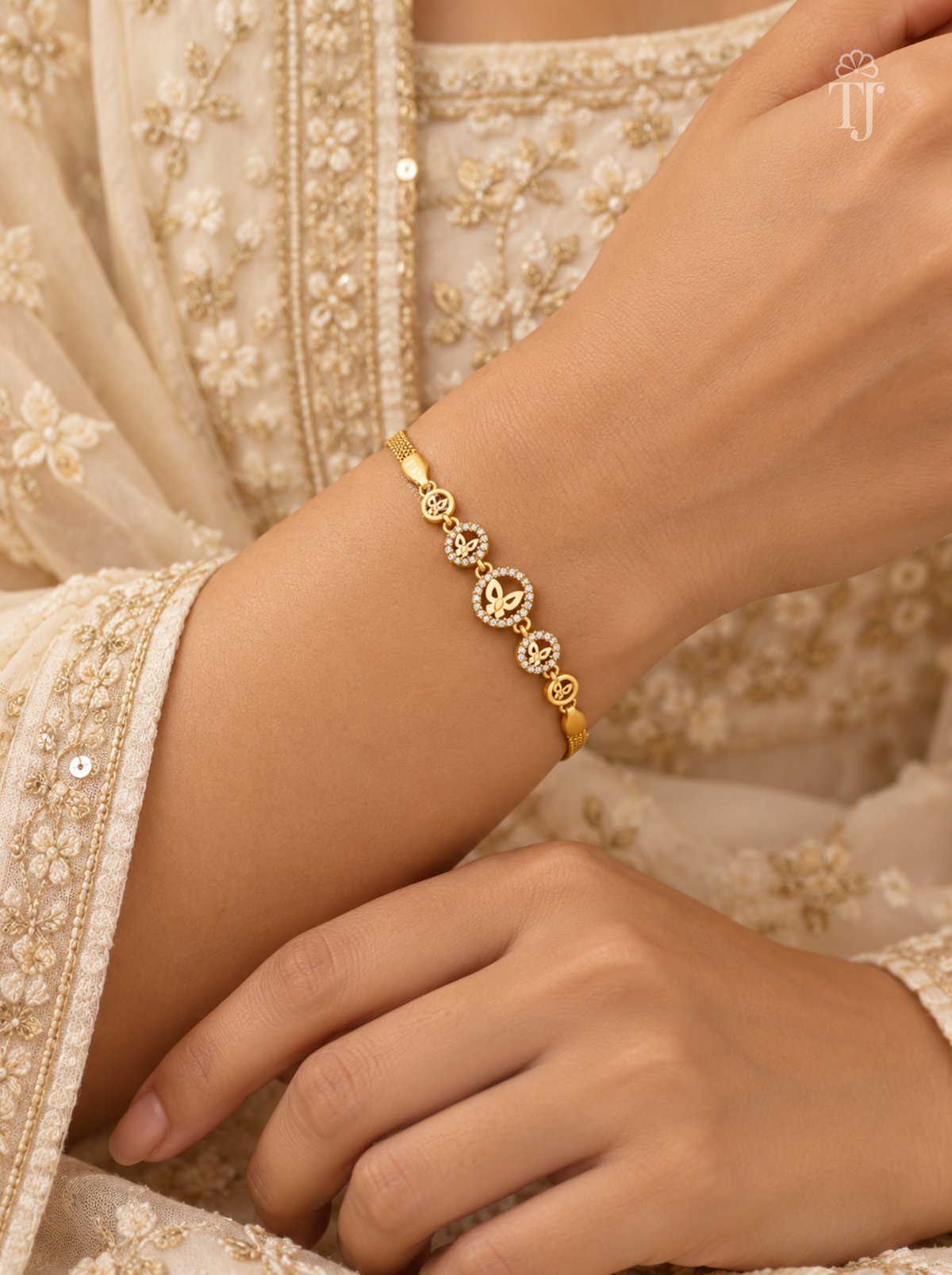A delicate gold bracelet with circular floral motifs worn on a woman's wrist, paired with a cream-colored embroidered traditional outfit.
