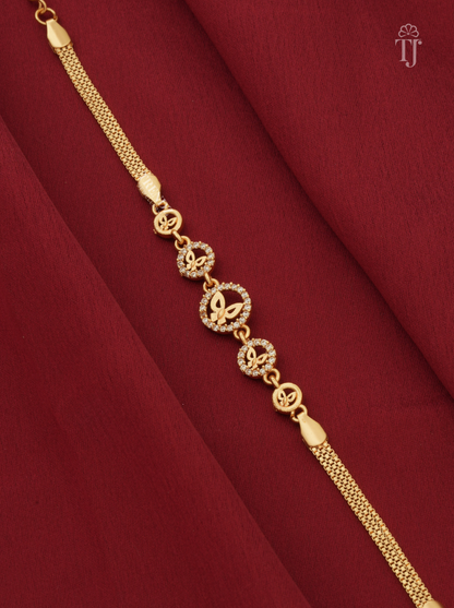 A gold chain bracelet with circular butterfly and monogram motifs, displayed diagonally on a draped dark red fabric background.