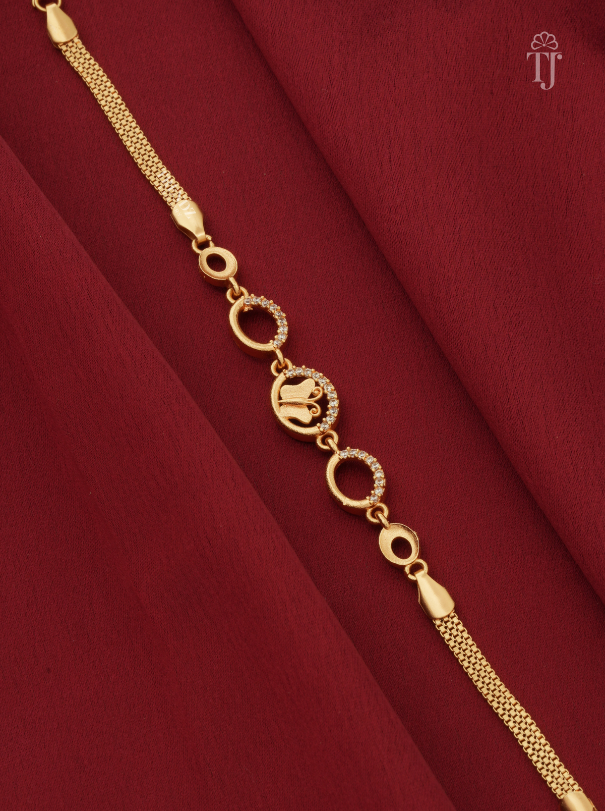 A gold-plated bracelet with a mesh chain, circular links, and a central elephant motif charm, displayed on a deep red fabric background.