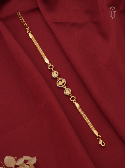 A gold-toned chain bracelet with five heart-shaped charms, each adorned with small clear stones, displayed diagonally on a draped dark red fabric background.