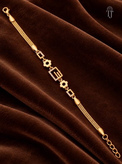 A gold chain bracelet with geometric and floral motifs, displayed diagonally on a draped brown velvet fabric background.