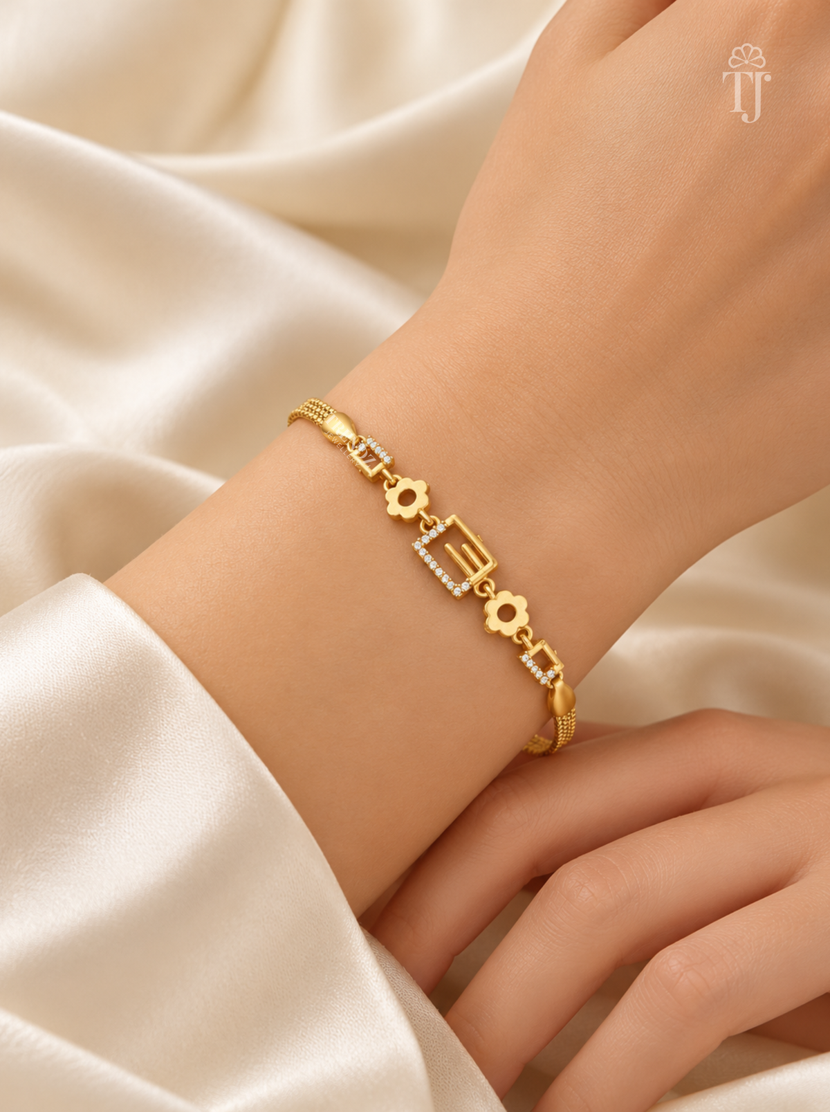 A gold bracelet with geometric and floral motifs, worn on a woman's wrist. The bracelet features a central rectangular link with small clear stones, flanked by gold flower and square links.
