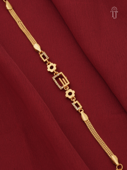 A gold-plated chain bracelet with geometric and floral motifs, some embellished with small clear stones, displayed diagonally on a draped dark red fabric background.