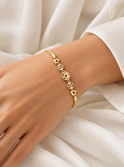 A delicate gold bracelet with a series of small heart and floral charms, worn on a woman's wrist against a soft, draped white fabric background.