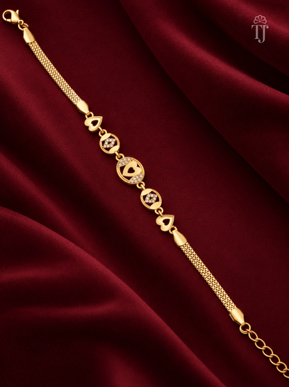 A gold chain bracelet with heart-shaped charms and small clear stones, displayed diagonally on a draped deep red satin fabric background.