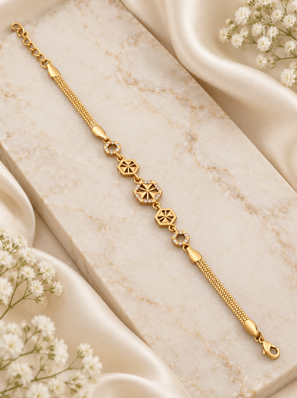 A gold chain bracelet with three central starburst charms and small clear stone accents, displayed on a cream marble block with white satin and baby's breath flowers.
