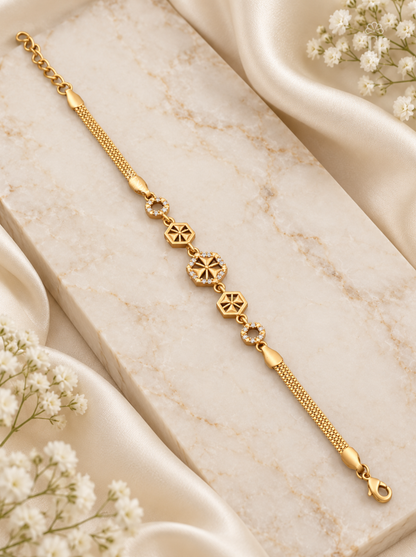 A gold chain bracelet with three central starburst charms and small clear stone accents, displayed on a cream marble block with white satin and baby's breath flowers.