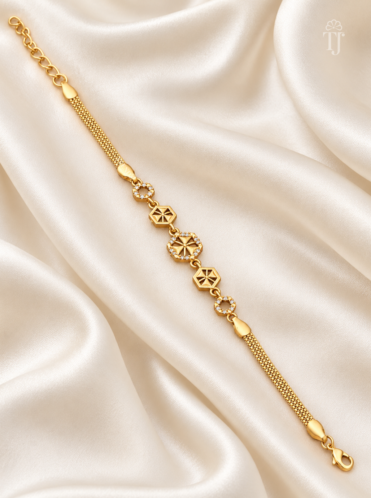 A gold chain bracelet with geometric and floral motifs, displayed diagonally on draped cream satin fabric.