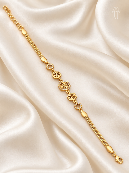 A gold chain bracelet with geometric and floral motifs, displayed diagonally on draped cream satin fabric.