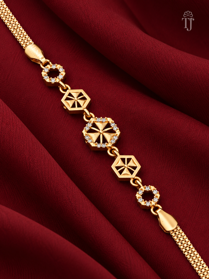 A gold-toned chain bracelet with geometric star and circular link motifs, some accented with small clear stones, displayed on draped deep red fabric.