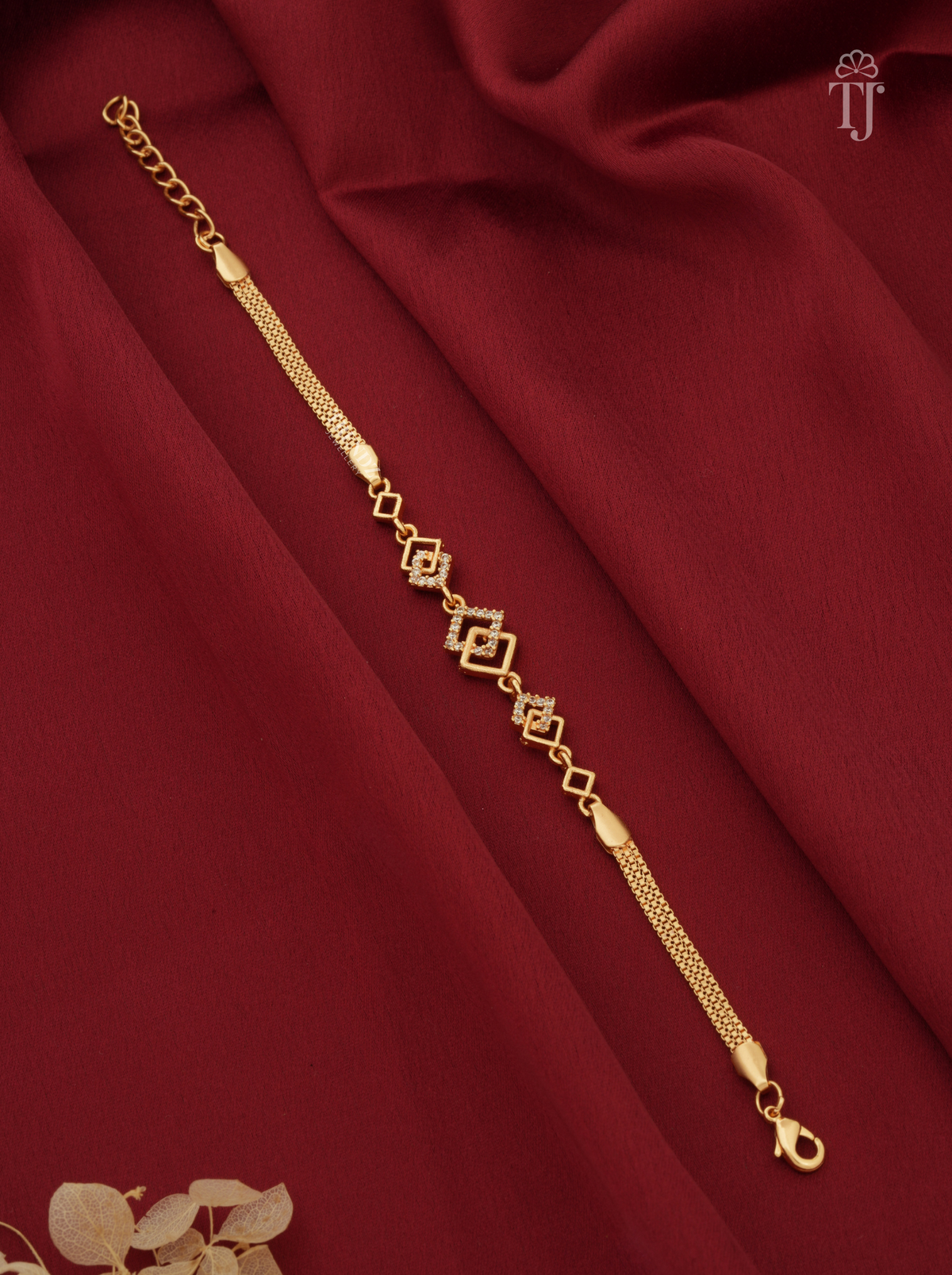 A gold-toned chain bracelet with repeating diamond-shaped links and a textured chain section, displayed diagonally on draped deep red fabric.
