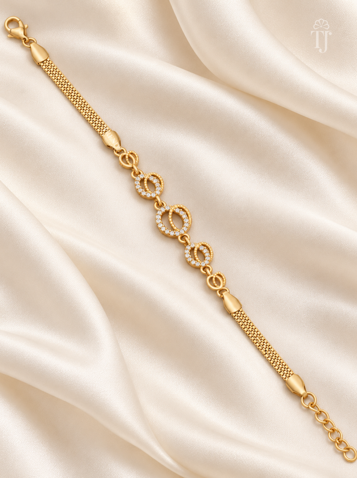 A gold chain bracelet with three interlocking circular links, two of which are adorned with small clear stones, displayed on a draped cream satin fabric.