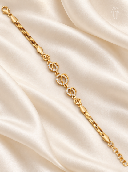 A gold chain bracelet with three interlocking circular links, two of which are adorned with small clear stones, displayed on a draped cream satin fabric.