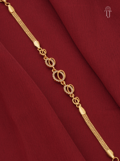 A gold chain bracelet with three oval links encrusted with small clear stones, displayed diagonally on draped deep red fabric.